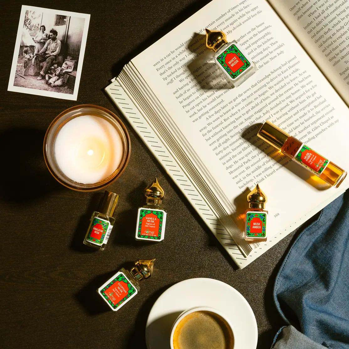 Nemat Perfume oil bottles with green labels on a surface with a lit candle and open book.