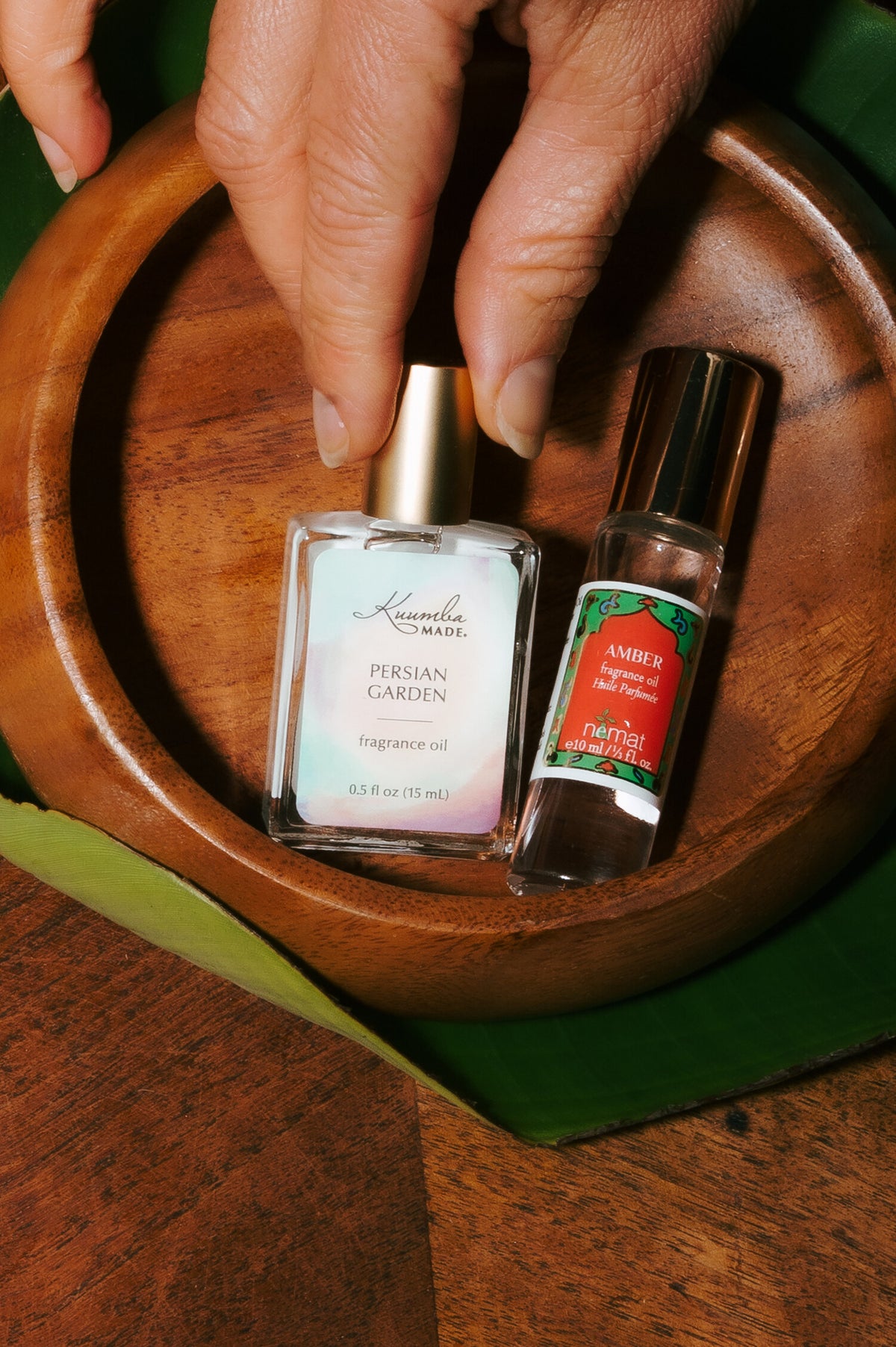 Kuumba Made Persian Garden and Nemat Amber perfume oils in a wooden bowl on a banana leaf